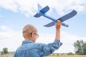 portret van een gelukkig kind spelen met een speelgoed- vliegtuig tegen een blauw lucht in een Open veld- foto