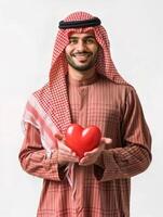 ai gegenereerd vrij foto van een jong Arabisch Mens weraing traditioneel kleren Holding een rood hart in zijn handen, geïsoleerd achtergrond