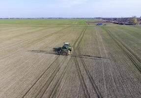 trekker met scharnierend systeem van sproeien pesticiden. bemesting met een tractor, in de het formulier van een aërosol, Aan de veld- van winter tarwe. foto