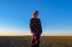 vrouw in een geploegd veld- in een rood Zwart jurk Aan een zonsondergang achtergrond. foto