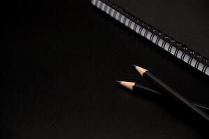 zwart potloden met zwart spiraal notitieboekje Aan zwart achtergrond. foto