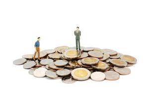twee miniatuur mensen wandelen en staand Aan stapel van nieuw Thais baht munten, geïsoleerd Aan wit achtergrond. bedrijf en financiën concept. foto