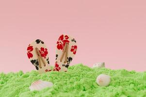 luxe magisch zomer lay-out gemaakt met bloemen slippers, groen strand zand en zee schelpen tegen licht roze achtergrond. minimaal concept. creatief fantasie strand idee. zomer esthetisch achtergrond. foto