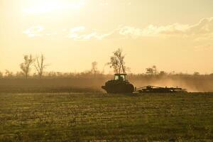 trekker Bij zonsondergang ploeg ploeg een veld. bewerken de bodem in de vallen na oogst. de einde van de seizoen foto