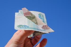 denominaties van Russisch geld, gevouwen in de vliegtuig tegen de blauw lucht in hand- foto