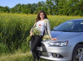 een mooi jong vrouw met een boeket van madeliefjes staat in de buurt een zilver auto foto