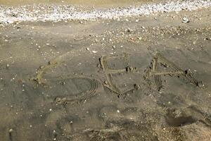 de opschrift van de zee Aan de zand. kust- zand en golven. inscripties Aan de kust foto