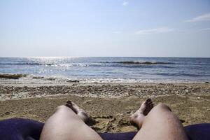 de poten van een Mens Aan een strand achtergrond. een Mens leugens Aan een amatras Aan de strand en is rusten. poten in de kader. foto