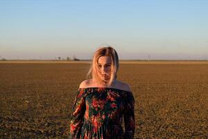 vrouw in een geploegd veld- in een rood Zwart jurk Aan een zonsondergang achtergrond. foto