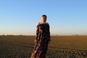 vrouw in een geploegd veld- in een rood Zwart jurk Aan een zonsondergang achtergrond. foto