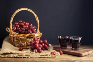 rood druif sap in een glas geplaatst Aan een houten tafel of rood wijn, een heerlijk natuurlijk gezond sap drankje. met een bundel van vers rood druiven van de tuin foto
