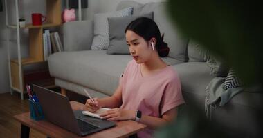 portret van jong vrouw zittend Aan de verdieping leunend tegen een sofa werken met een laptop en nemen aantekeningen in een notitieboekje Bij huis kantoor. foto