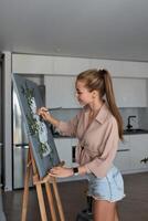 een creatief vrouw artiest staat en werken Aan een schilderen. een gelukkig jong dame is schilderij Aan canvas in haar appartement. de concept van een jong moeder vrije tijd foto