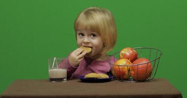 meisje zittend Bij de tafel met appels, cacao en aan het eten koekjes. chroma sleutel foto