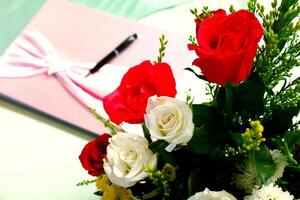 vers wit en rood roos bloem boeket met wazig mooi roze boek of notitieboekje en zwart pen of potlood voor achtergrond. bruiloft viering, mooi zo geheugen boek en schoonheid van natuur. foto