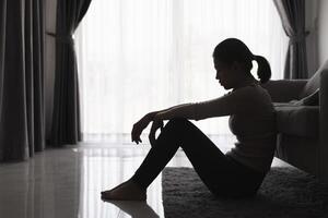 silhouet van een persoon lijden van depressie in de huis, depressief vrouw zittend alleen Aan de sofa voelen spanning, verdrietig en bezorgd in de donker kamer. persoon zijn benadrukt. foto