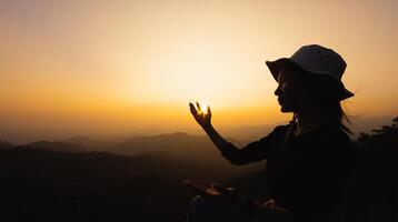 silhuette jong vrouw bidden Aan de berg, armen uitgestrekt observeren een mooi dramatisch zonsopkomst. foto