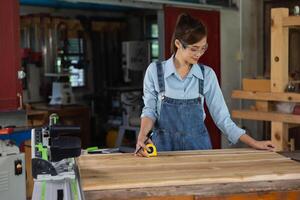 jong vrouw is opleiding naar worden een timmerman in werkplaats. timmerman werken met uitrusting Aan houten tafel. vrouw werken in een timmerwerk winkel. foto