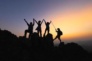 silhouet samenspel van vier wandelaar helpen elk andere Aan top van berg beklimming team mooi zonsopkomst. samenspel vriendschap wandelen helpen elk andere vertrouwen bijstand. beklimming team succes. foto