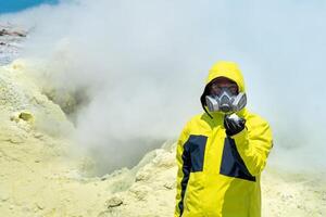 Mens vulkanoloog Aan de achtergrond van een roken fumarole demonstreert een monster van een mineraal foto