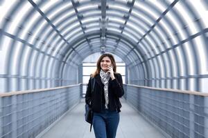 jong vrouw is wandelen snel langs de gedekt voetganger viaduct, pratend Aan de telefoon foto