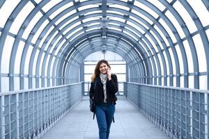 jong vrouw lachend terwijl pratend Aan de telefoon wandelen Aan de gedekt viaduct foto