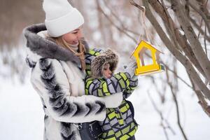 moeder en zoon in een winter park voeden vogelstand gebruik makend van een voeder foto