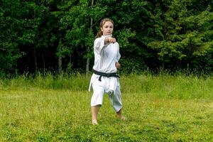 tiener- meisje opleiding karate kata buitenshuis, presteert stempel seiken chudan tsuki foto