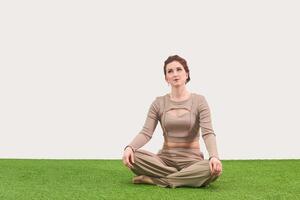 jong vrouw zittend in meditatie houding en looks omhoog dromerig Aan licht achtergrond foto