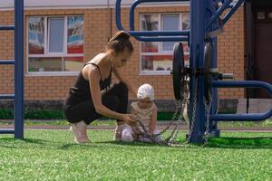 mam en kleuter dochter zijn wandelen Aan de sport- grond in de buurt de huis, de baby is geïnteresseerd in een oefening machine foto