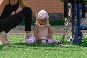 mam en kleuter dochter zijn wandelen Aan de sport- grond in de buurt de huis, de baby is geïnteresseerd in een oefening machine foto