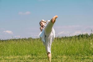 tiener- meisje opleiding karate kata buitenshuis, presteert de yoko geri trap met kiai foto