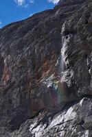 puur rots en een waterval met regenboog tegen de lucht foto