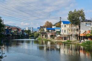de bank van de dagomys rivier- is gebouwd omhoog met klein huisjes met garages voor boten, hoogbouw gebouwen en bergen Aan de horizon in sochy, Rusland foto