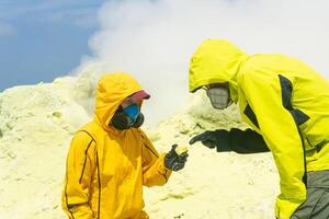 vulkanologen Aan de helling van de vulkaan onderzoekt monsters van mineralen tegen de backdrop van roken zwavel fumarolen foto