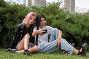 twee tiener- meisjes aan het kijken iets Aan een smartphone, schuilplaats achter struiken in een park foto