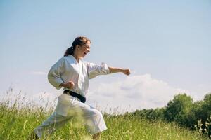 tiener meisje opleiding karate kata buitenshuis, het uitvoeren van een staking oi zuki gebruik makend van kiai foto