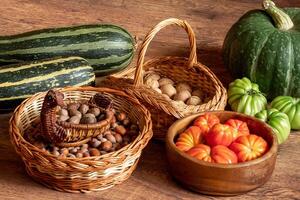 oogst van vers tomaten, pompoen en courgettes en manden met hazelnoten en walnoten gestapeld Aan de verdieping foto