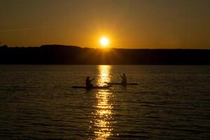 twee surfers Aan sta op paddleboards tegen de backdrop van de instelling zon foto