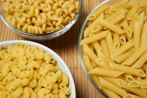 drie kommen van droog pasta Aan een riet tafelkleed, detailopname foto