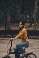 gelukkig jong Aziatisch vrouw terwijl rijden een fiets in een stad park. ze glimlachte gebruik makend van de fiets van vervoer. milieuvriendelijk vriendelijk concept. foto