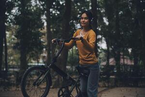 gelukkig jong Aziatisch vrouw terwijl rijden een fiets in een stad park. ze glimlachte gebruik makend van de fiets van vervoer. milieuvriendelijk vriendelijk concept. foto