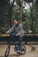 gelukkig Aziatisch jong vrouw wandelen en rijden fiets in park, straat stad haar glimlachen gebruik makend van fiets van vervoer, eco vriendelijk, mensen levensstijl concept. foto