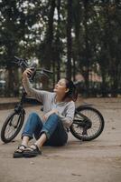 gelukkig Aziatisch jong vrouw wandelen en rijden fiets in park, straat stad haar glimlachen gebruik makend van fiets van vervoer, eco vriendelijk, mensen levensstijl concept. foto