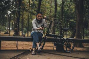 gelukkig Aziatisch jong vrouw wandelen en rijden fiets in park, straat stad haar glimlachen gebruik makend van fiets van vervoer, eco vriendelijk, mensen levensstijl concept. foto