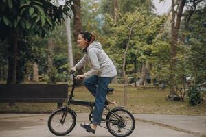 gelukkig Aziatisch jong vrouw wandelen en rijden fiets in park, straat stad haar glimlachen gebruik makend van fiets van vervoer, eco vriendelijk, mensen levensstijl concept. foto