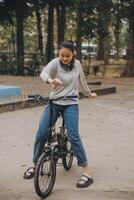 gelukkig Aziatisch jong vrouw wandelen en rijden fiets in park, straat stad haar glimlachen gebruik makend van fiets van vervoer, eco vriendelijk, mensen levensstijl concept. foto