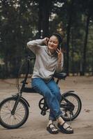 gelukkig Aziatisch jong vrouw wandelen en rijden fiets in park, straat stad haar glimlachen gebruik makend van fiets van vervoer, eco vriendelijk, mensen levensstijl concept. foto