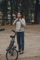 gelukkig Aziatisch jong vrouw wandelen en rijden fiets in park, straat stad haar glimlachen gebruik makend van fiets van vervoer, eco vriendelijk, mensen levensstijl concept. foto