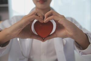 handen van dokter vrouw Holding rood hart, tonen symbool van liefde, menselijk ondersteuning naar geduldig, bevorderen medisch verzekering, vroeg controle voor gezondheidszorg, cardioloog helpen. dichtbij omhoog van voorwerp foto